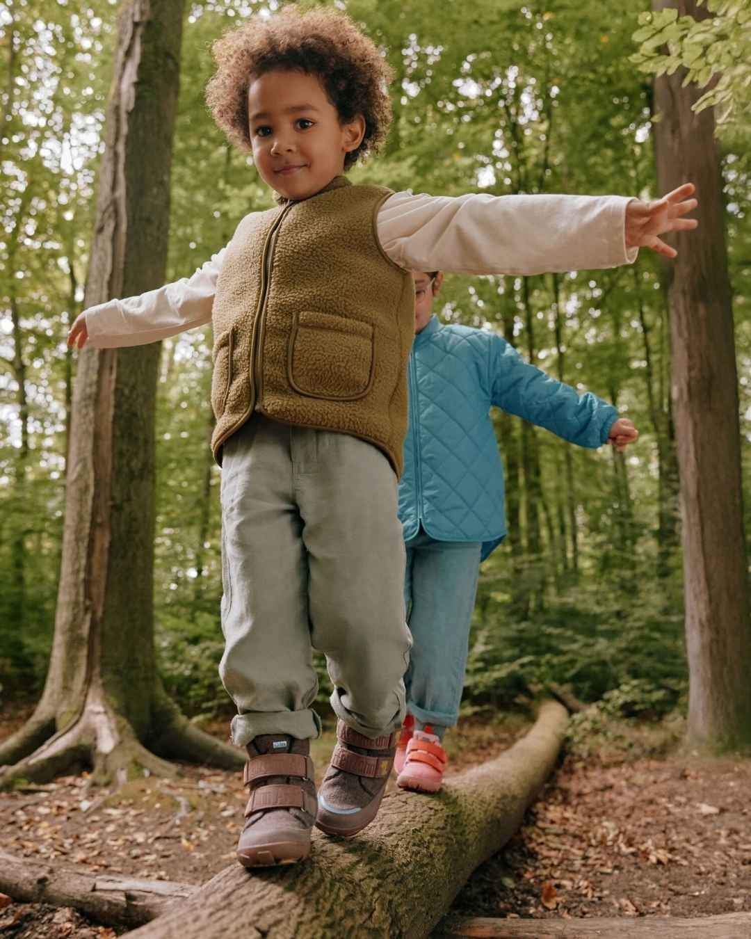 Mädchen und Jungen balancieren im wald über umgestürtzten baumstamm- tragen affenzahn schuhe