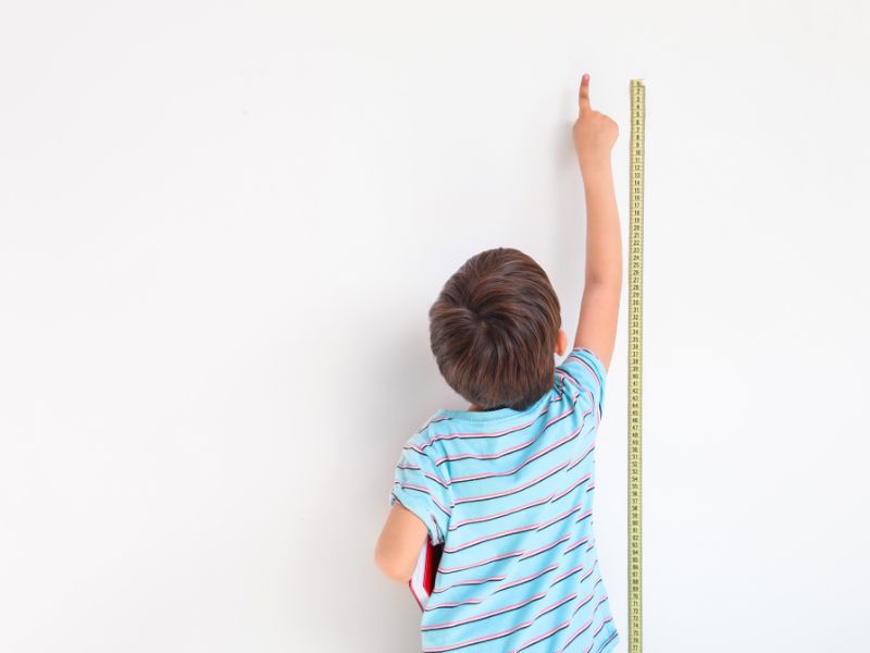 kleiner junge für richter kinderschuhe kleiner Junge reckt sich vor Maßband an der Wand