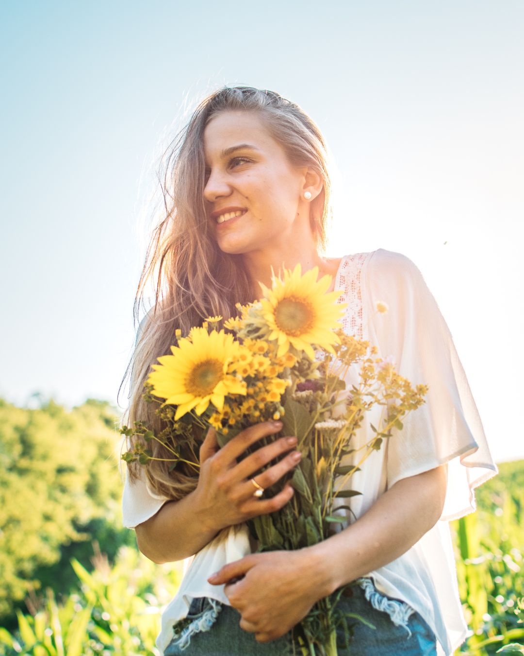 Frau mit sonnenblumen im arm steht in Sonnenblumenfeld