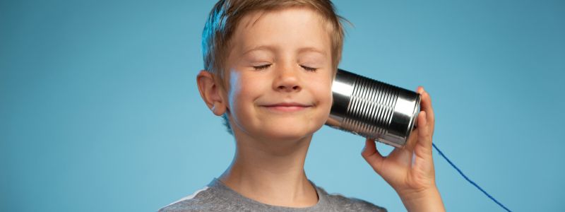Junge hält Dose von Schnurtelefon an sein Ohr und lauscht