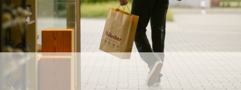 Kunde verlässt mit Schuh Hölscher Tragetasche das Geschäft
